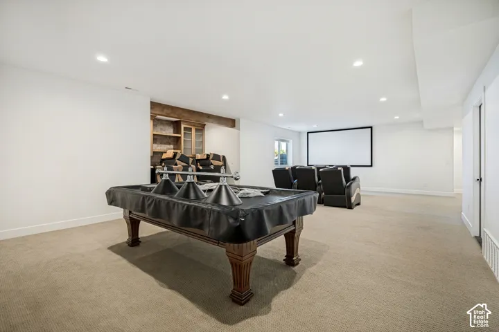 Spacious finished basement with recessed lighting, integrated projection screen, and built-in shelving with wood finish
