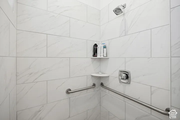 White subway tile shower surround with subtle veining, chrome shower head, chrome shower control, integrated corner shelving, and stainless steel grab bars