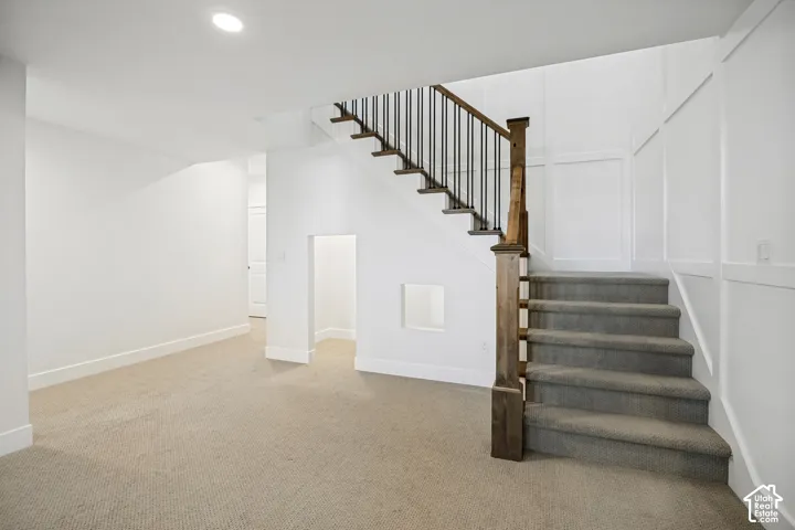 Plush carpeting, recessed lighting, and a staircase featuring wood newel posts and metal spindles