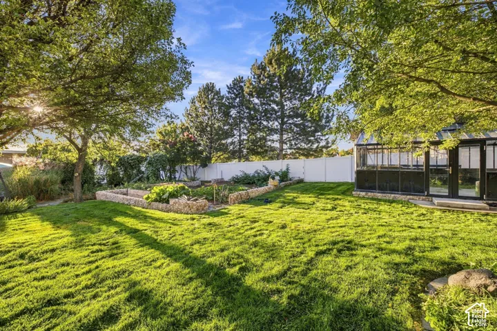 Expansive lawn with mature trees, raised stone garden beds, and a glass-paneled greenhouse with double doors