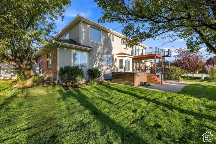 Expansive rear lawn with established trees, multi-level deck, and a ground-level patio with an integrated spa