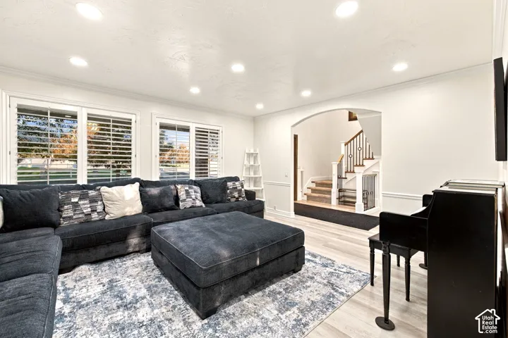 Recessed lighting, wood-finish flooring, white plantation shutters, arched doorway, and a staircase with decorative metal balusters
