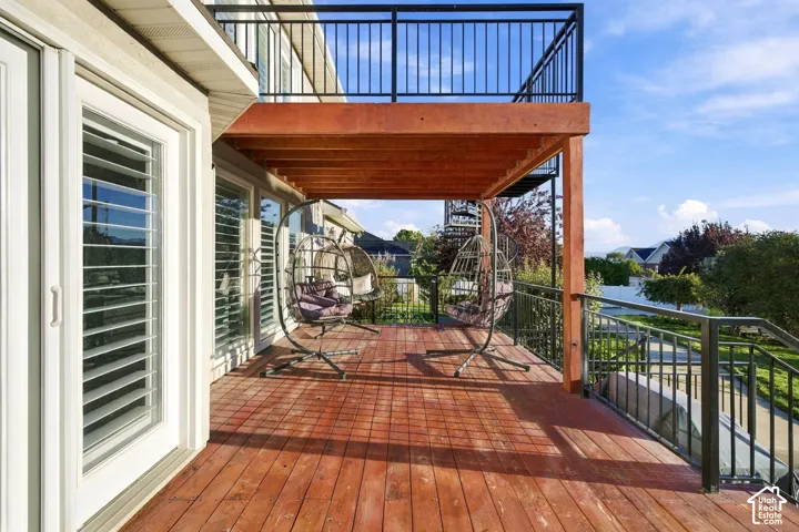 Expansive outdoor deck with rich wood flooring, black metal railings, and a sheltered patio beneath an upper-level balcony