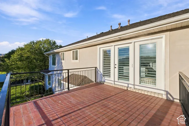Spacious exterior deck with brick-patterned flooring, black metal railing, and white double French doors with interior plantation shutters
