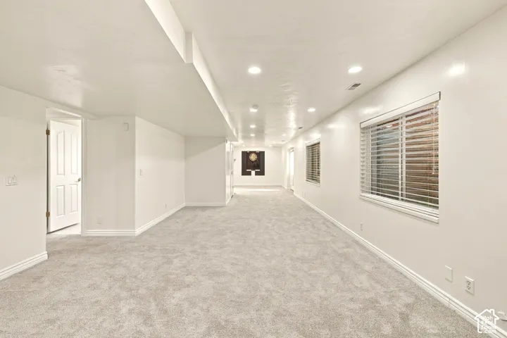 Spacious room with light-colored carpeting, multiple recessed lights, and two windows with blinds