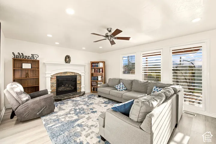 Living area featuring a white mantel fireplace with a stone surround, recessed lighting, wood-finish flooring, and white plantation shutters