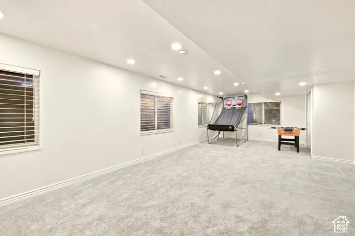 Spacious room featuring light-colored carpeting, multiple windows with blinds, recessed lighting, and white walls