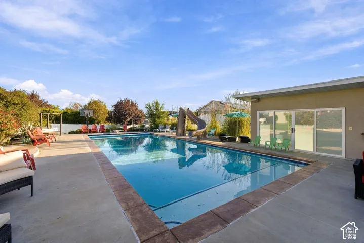 Inground swimming pool with integrated slide, concrete surround, and adjacent building with sliding glass doors