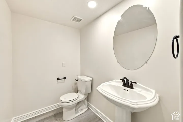 Pedestal sink with dark bronze faucet, oval mirror, and wood-finish flooring