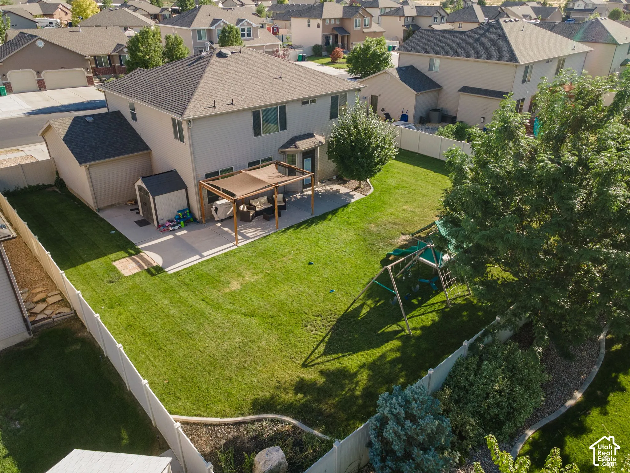 Expansive backyard featuring a large green lawn, concrete patio, and a shaded pergola structure