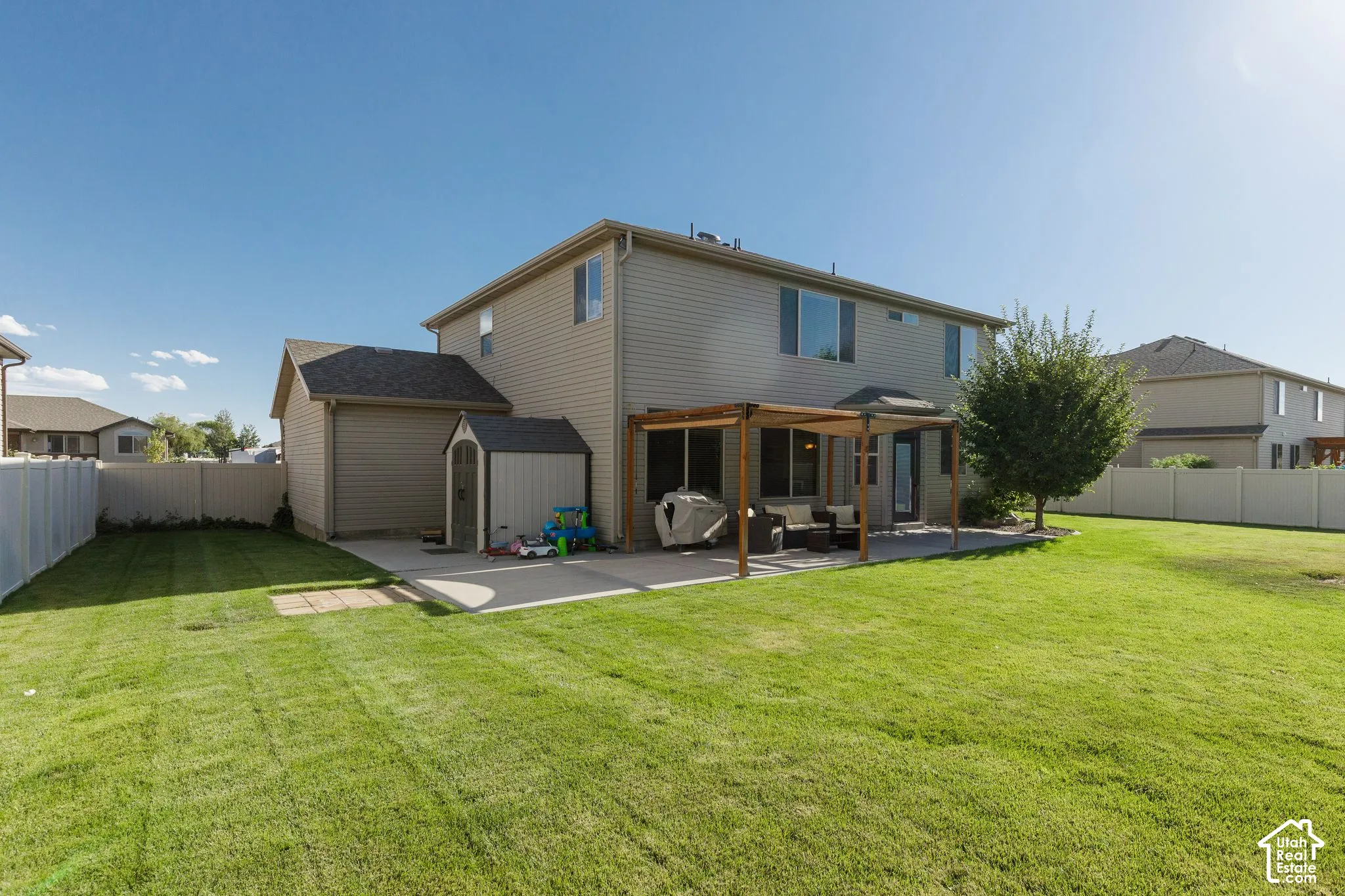 Expansive backyard featuring a manicured lawn, concrete patio with a wood pergola, and mature landscaping