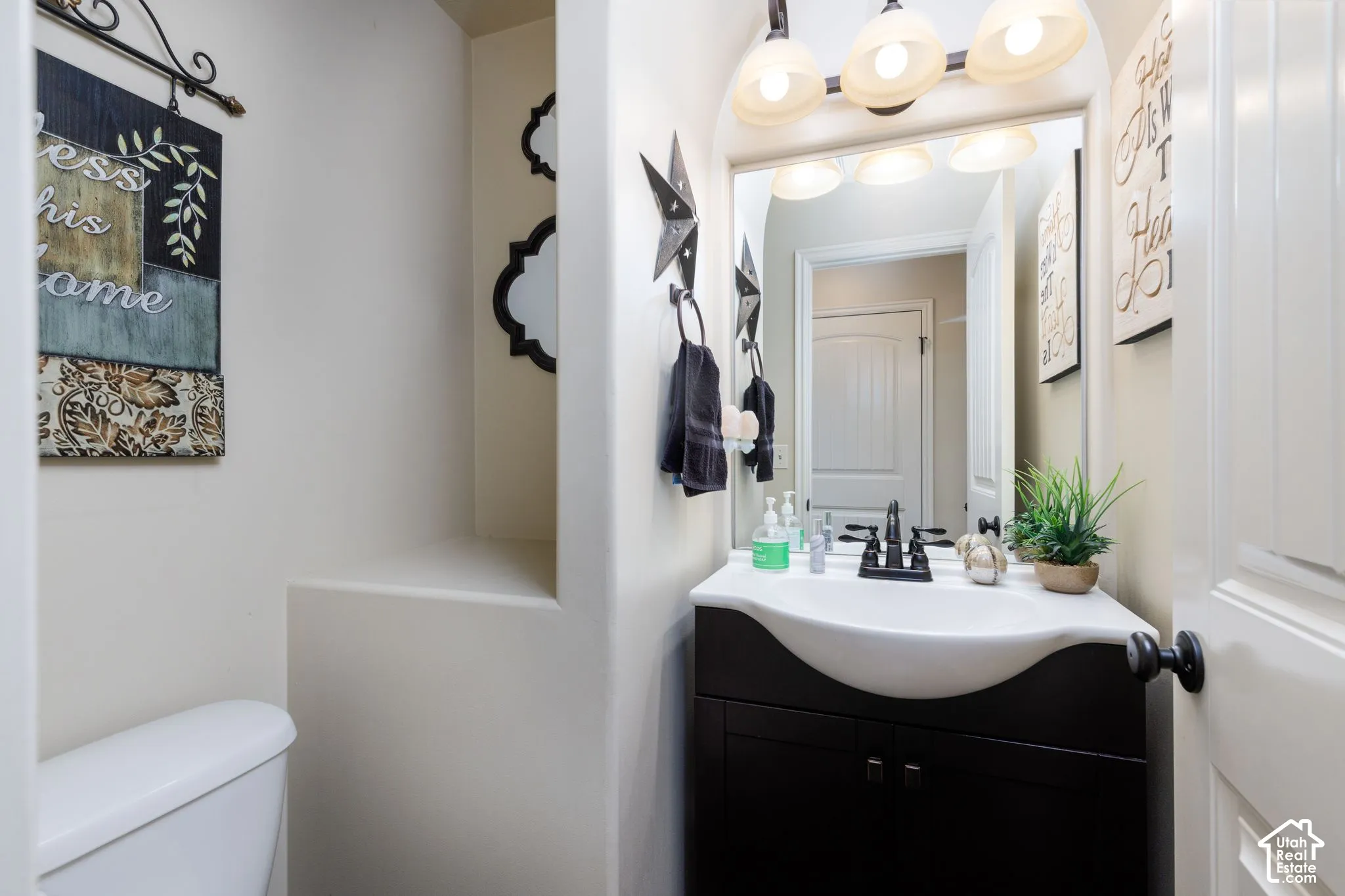 White toilet, dark wood-finish vanity with integrated white sink, wall-mounted vanity mirror, and three-light vanity fixture