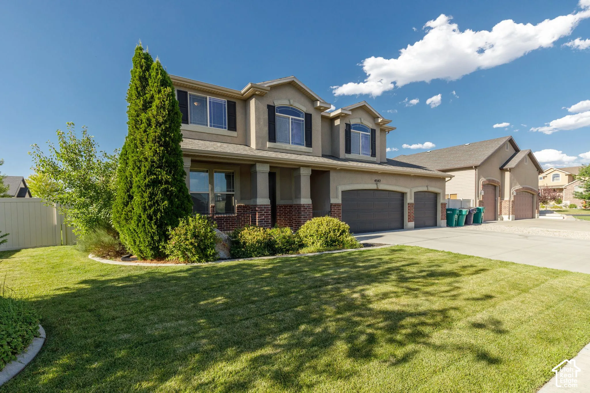 Two-story stucco exterior with brick accents, prominent two-car garage, multiple upper-level windows with dark shutters, and a well-maintained front lawn