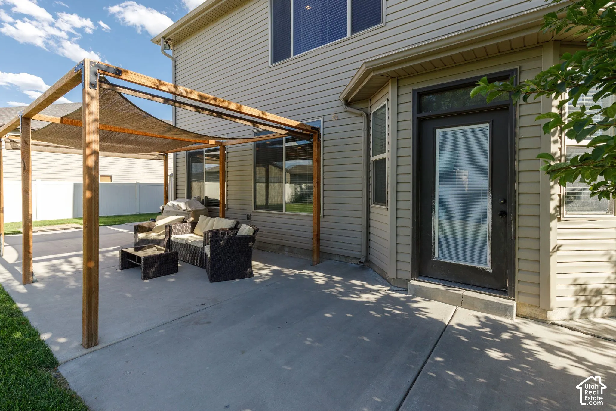 Concrete patio with a wood pergola and retractable shade canopy, featuring a full-light exterior door