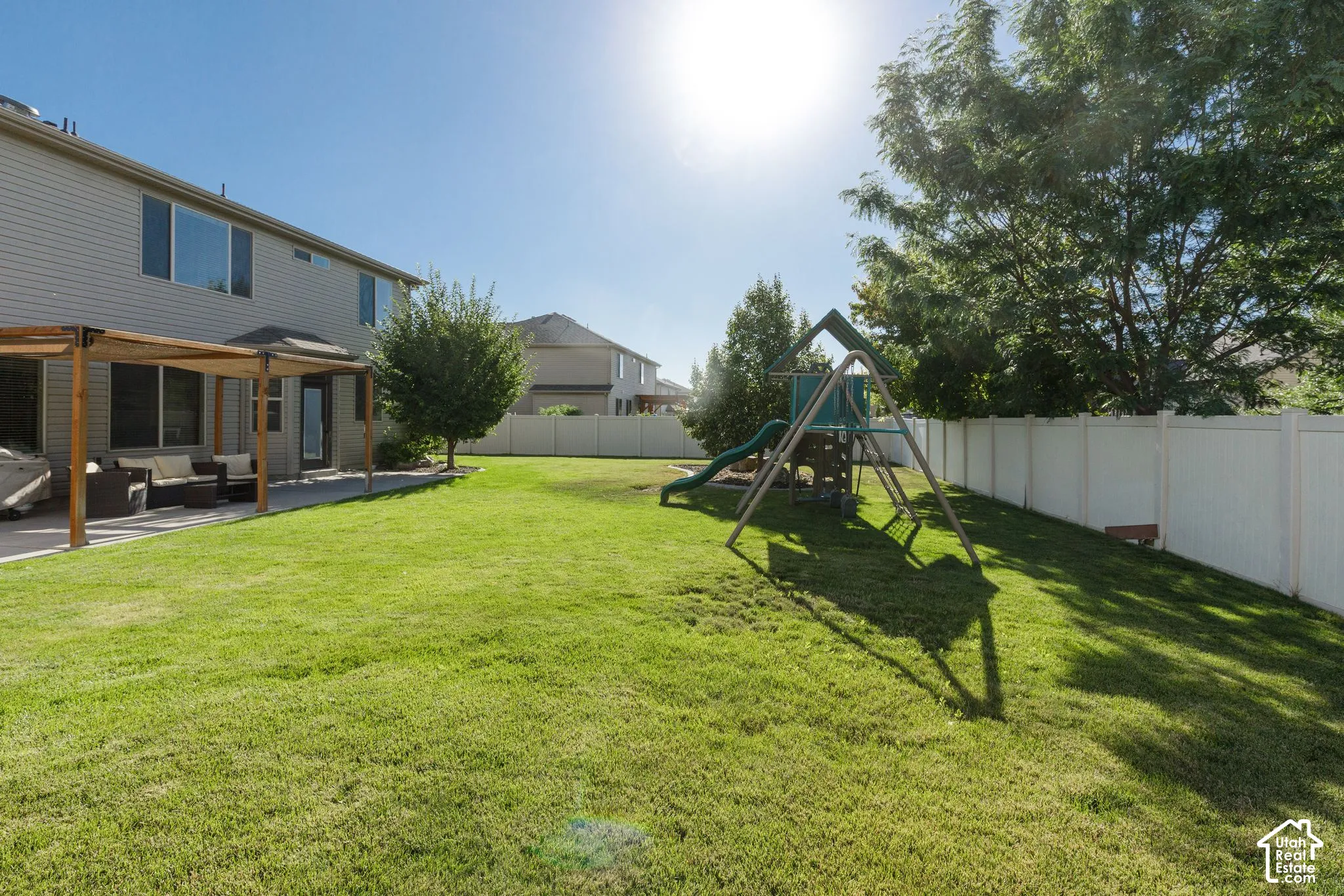 Expansive backyard featuring a lush lawn, a full-height privacy fence, and a concrete patio with a wooden pergola