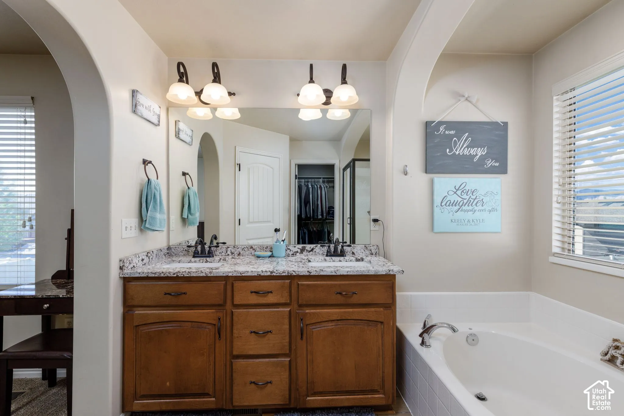 Dual vanity with granite-style countertop, wood-finish cabinetry, and an integrated soaking tub