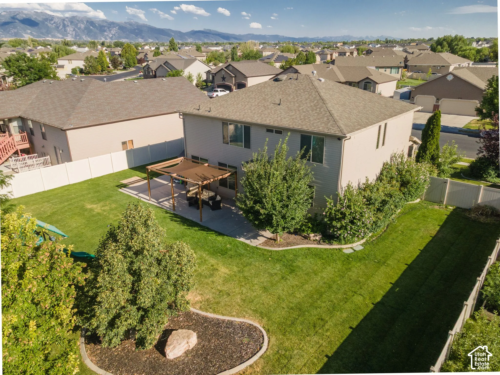 Expansive backyard featuring a manicured lawn, paved patio with pergola, and mature landscaping
