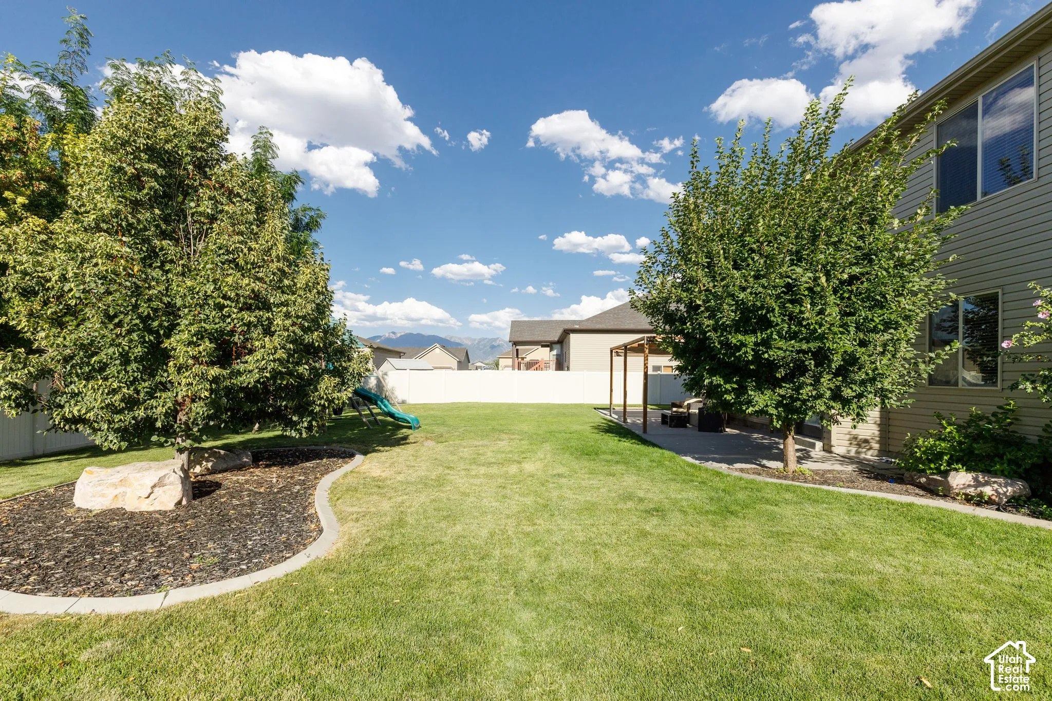 Expansive green lawn with mature trees, a concrete patio, and a wood pergola