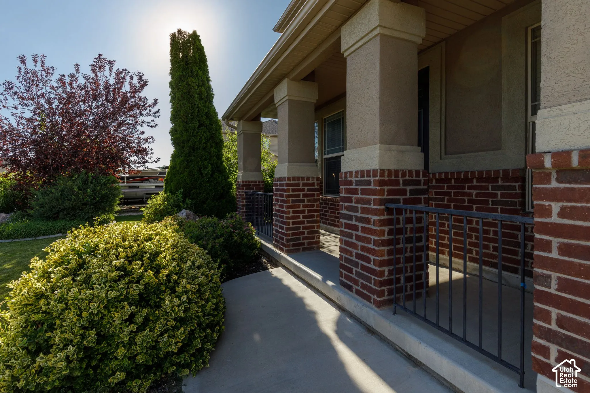 Front porch featuring brick and stucco columns, a concrete walkway, and a black metal railing