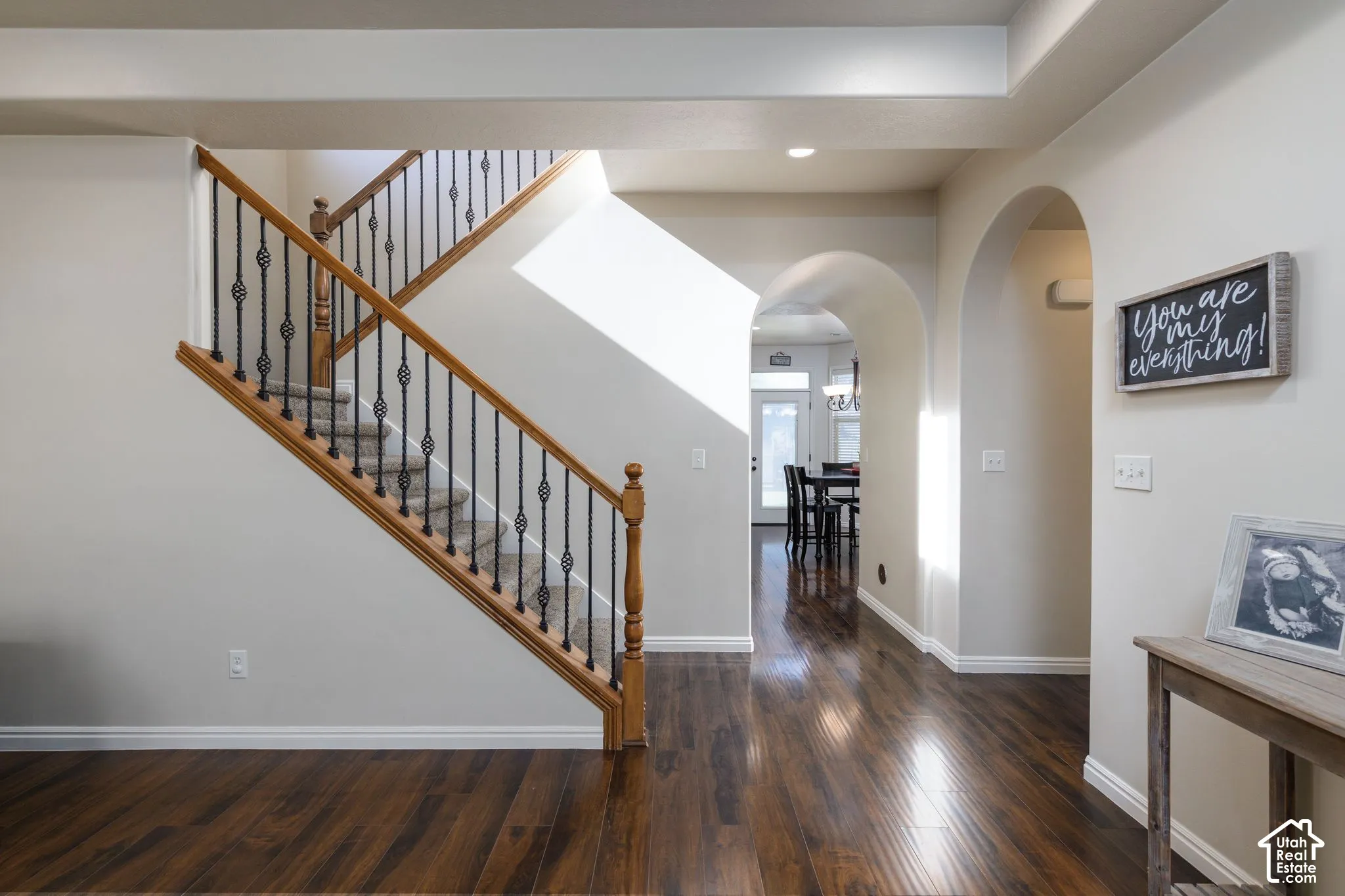 Hardwood-finish flooring, staircase with wood handrails and wrought iron balusters, recessed lighting, arched doorways, and tray ceiling