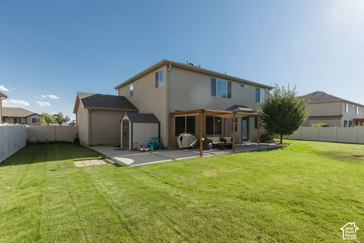 Expansive backyard featuring a manicured lawn, concrete patio with a wood pergola, and mature landscaping