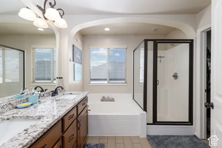 Double vanity with granite-style countertop, wood-finish cabinetry, built-in bathtub with tiled surround, and separate glass-enclosed shower