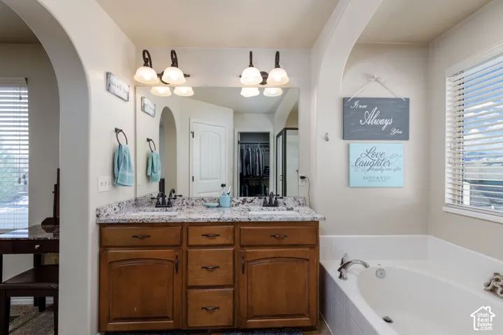Dual vanity with granite-style countertop, wood-finish cabinetry, and an integrated soaking tub