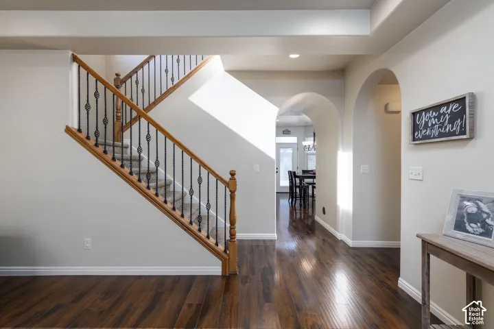 Hardwood-finish flooring, staircase with wood handrails and wrought iron balusters, recessed lighting, arched doorways, and tray ceiling