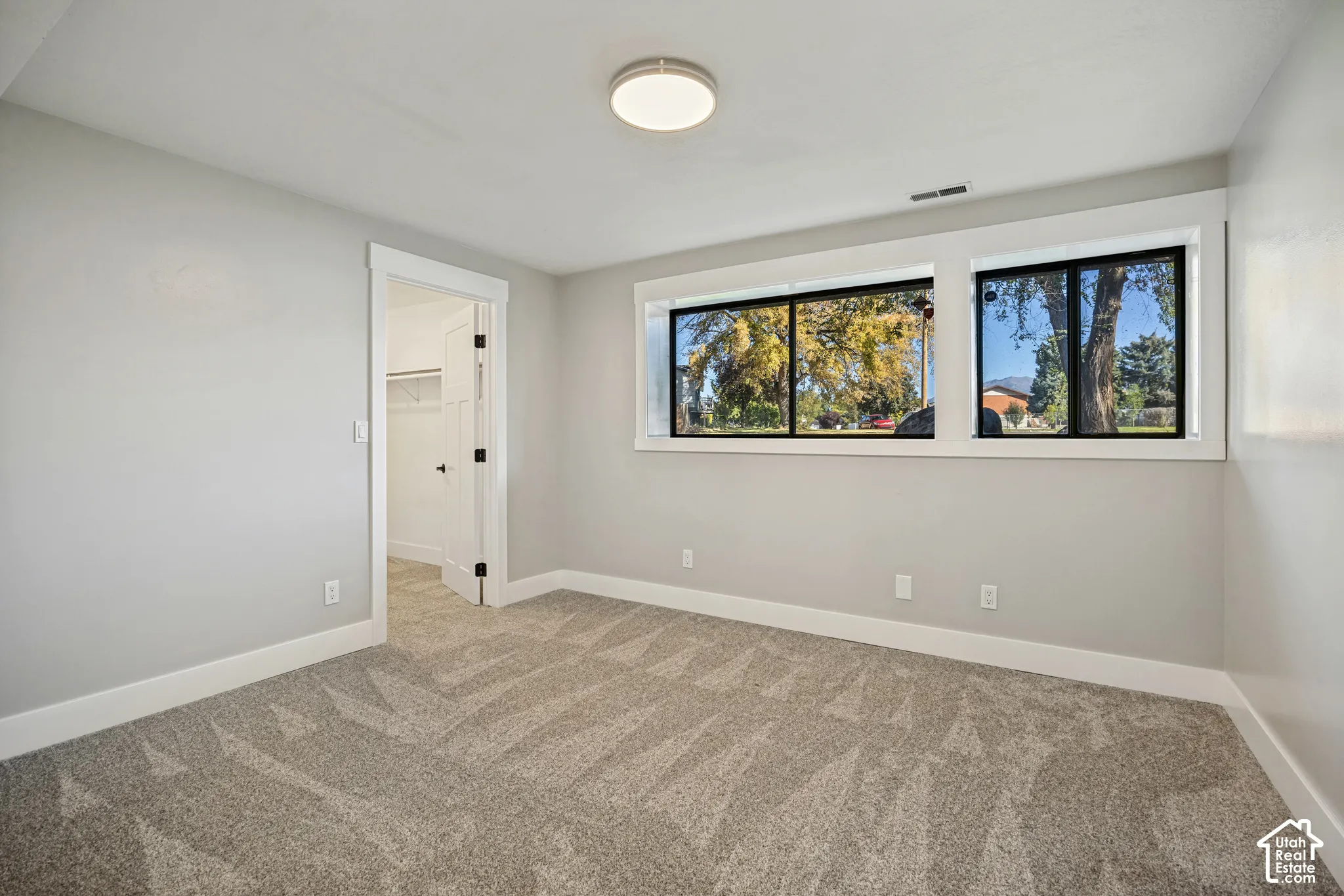 Spacious room featuring neutral paint, gray patterned carpet, a flush mount ceiling light, and two large windows with black frames