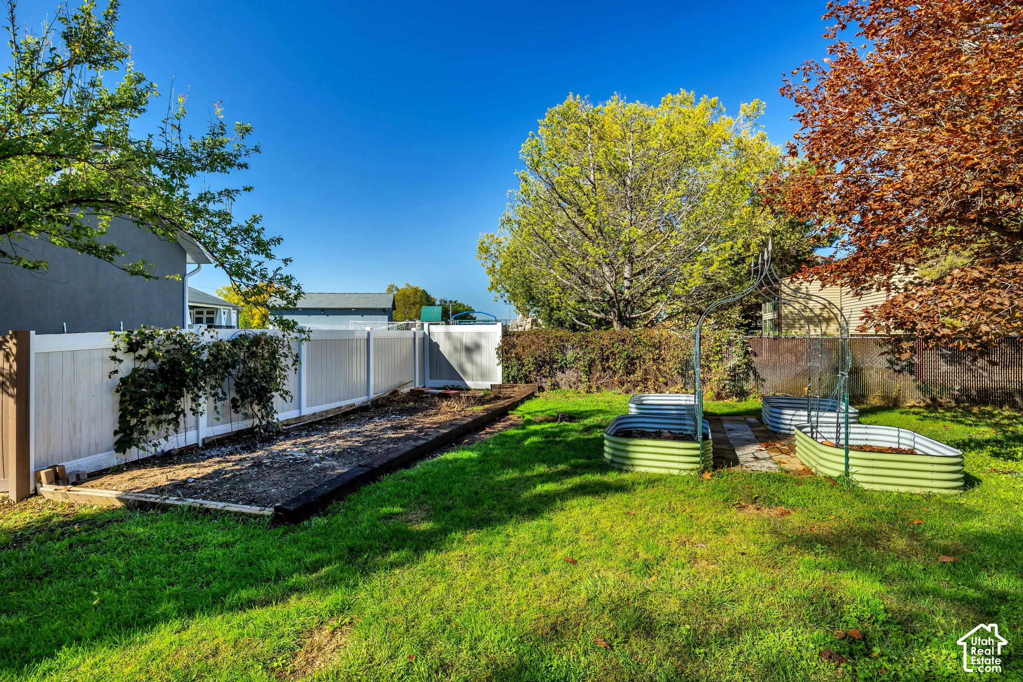 Expansive backyard featuring a manicured lawn, established garden beds, and a perimeter privacy fence with gate