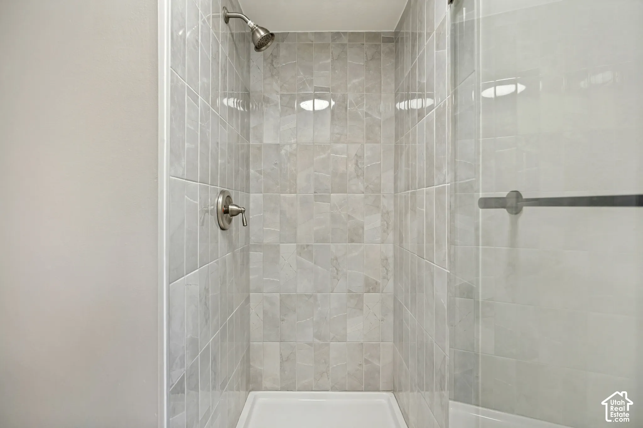 Tiled shower with brushed nickel fixtures, a glass shower enclosure, and a white shower base