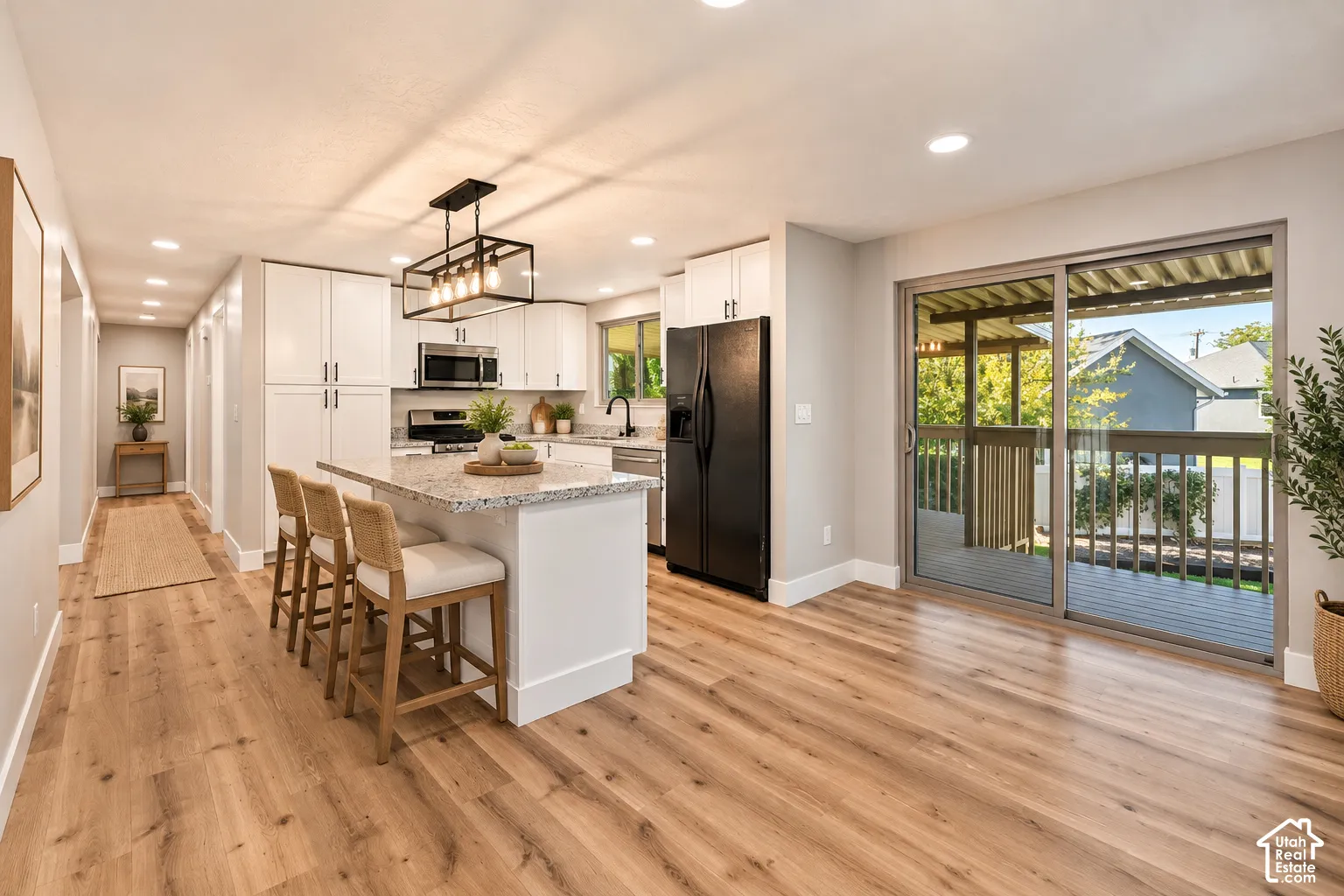Open-concept kitchen with white cabinetry, stainless steel appliances, a center island with a stone countertop, and wood-finish flooring