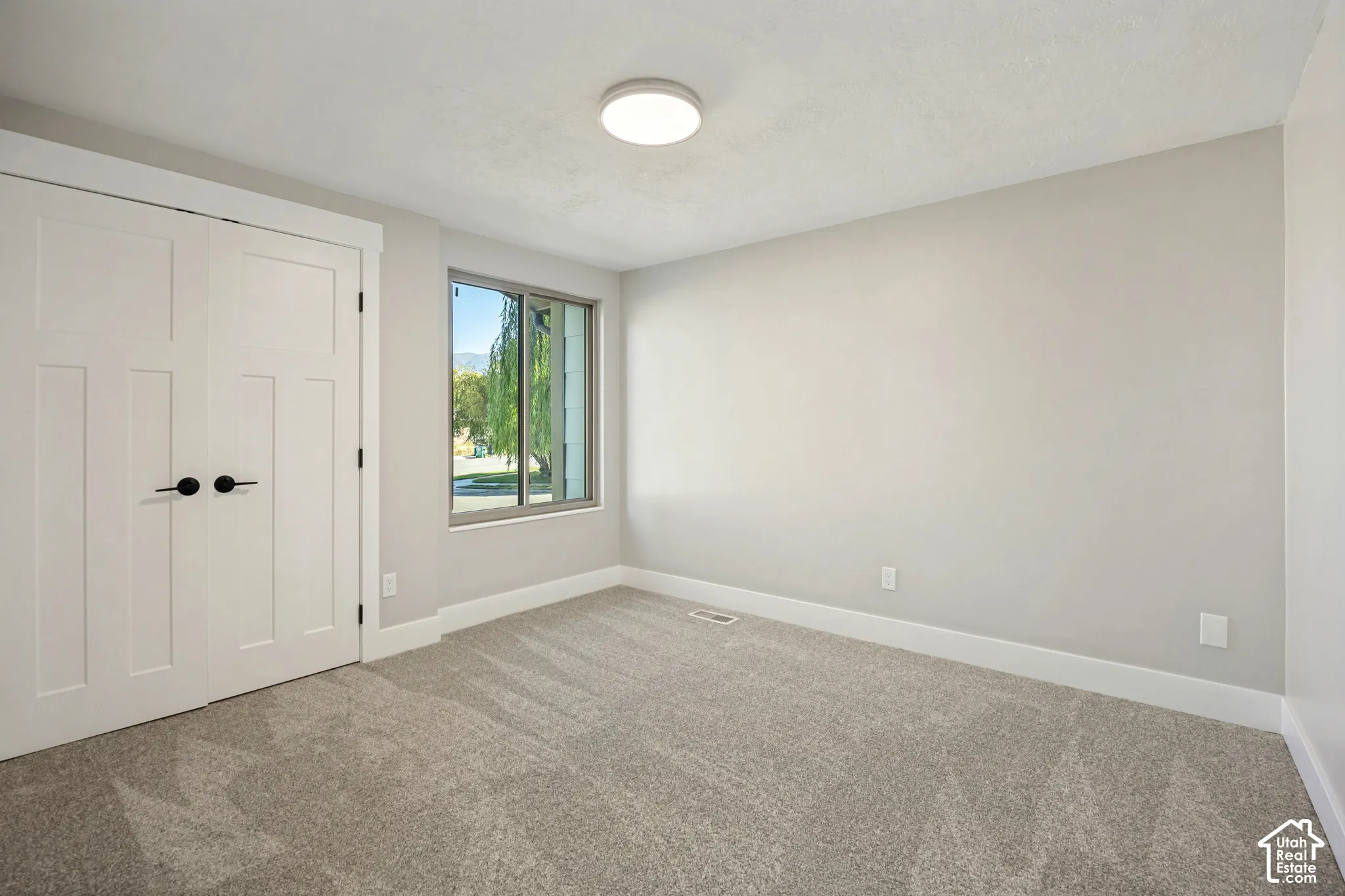 Neutral wall finishes, recessed window, light-colored carpet, white trim throughout, and a flush-mount ceiling light