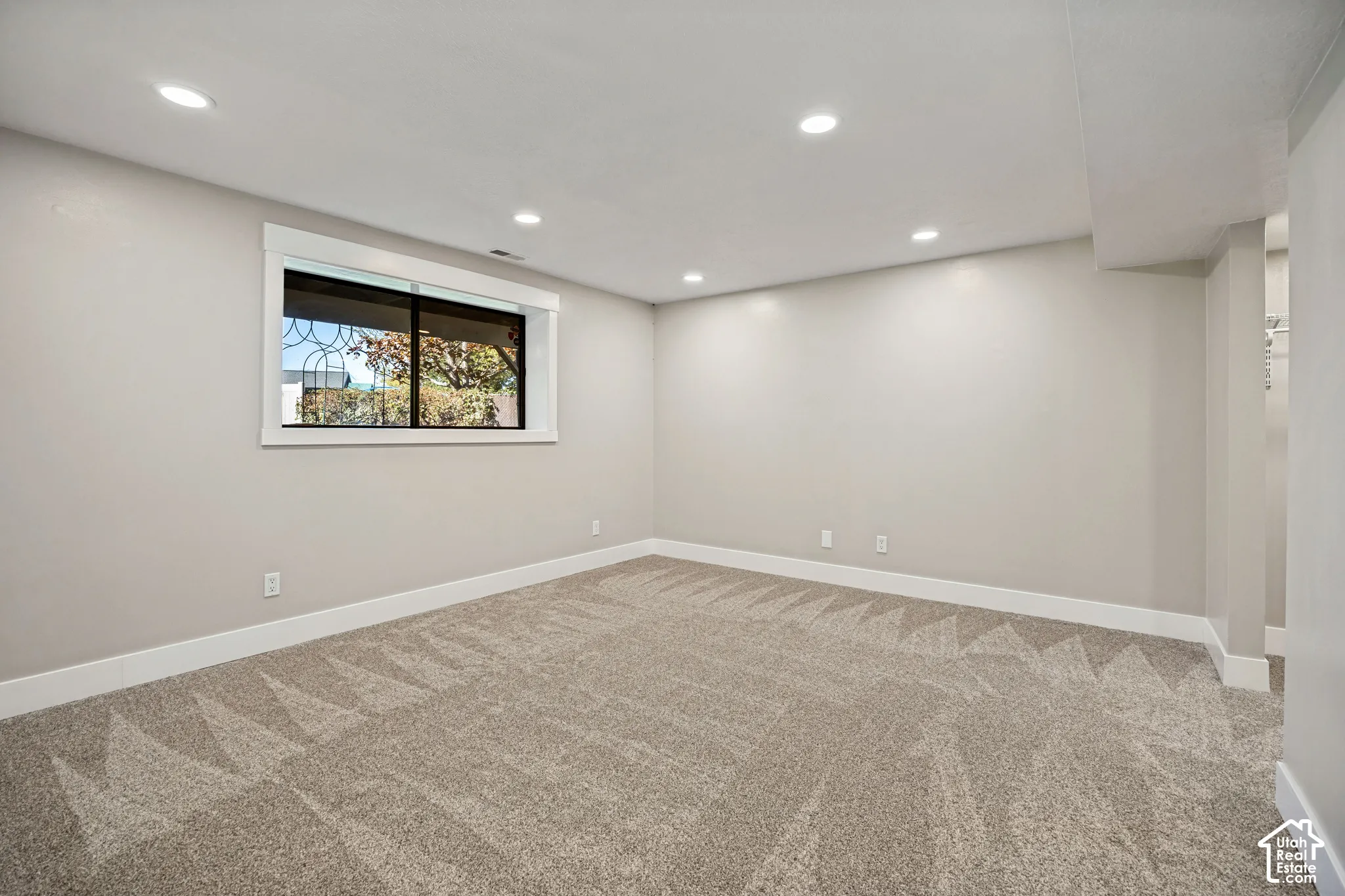 Recessed lighting, neutral wall tones, window with white trim, patterned carpeting, and white baseboards