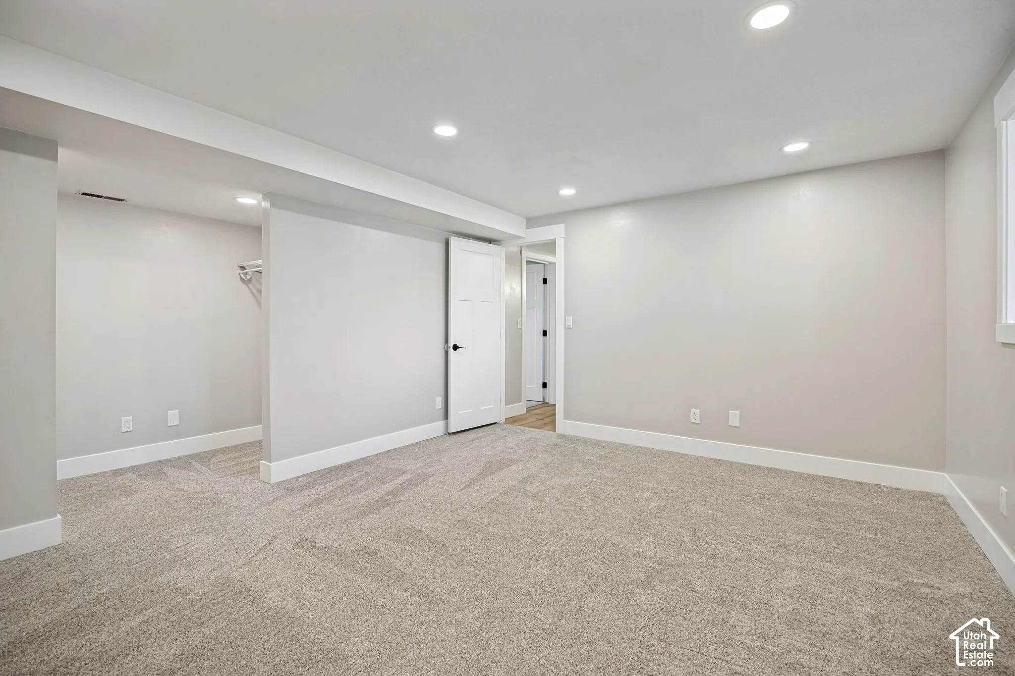 Spacious room with plush carpeting, recessed lighting, white trim, and a white interior door