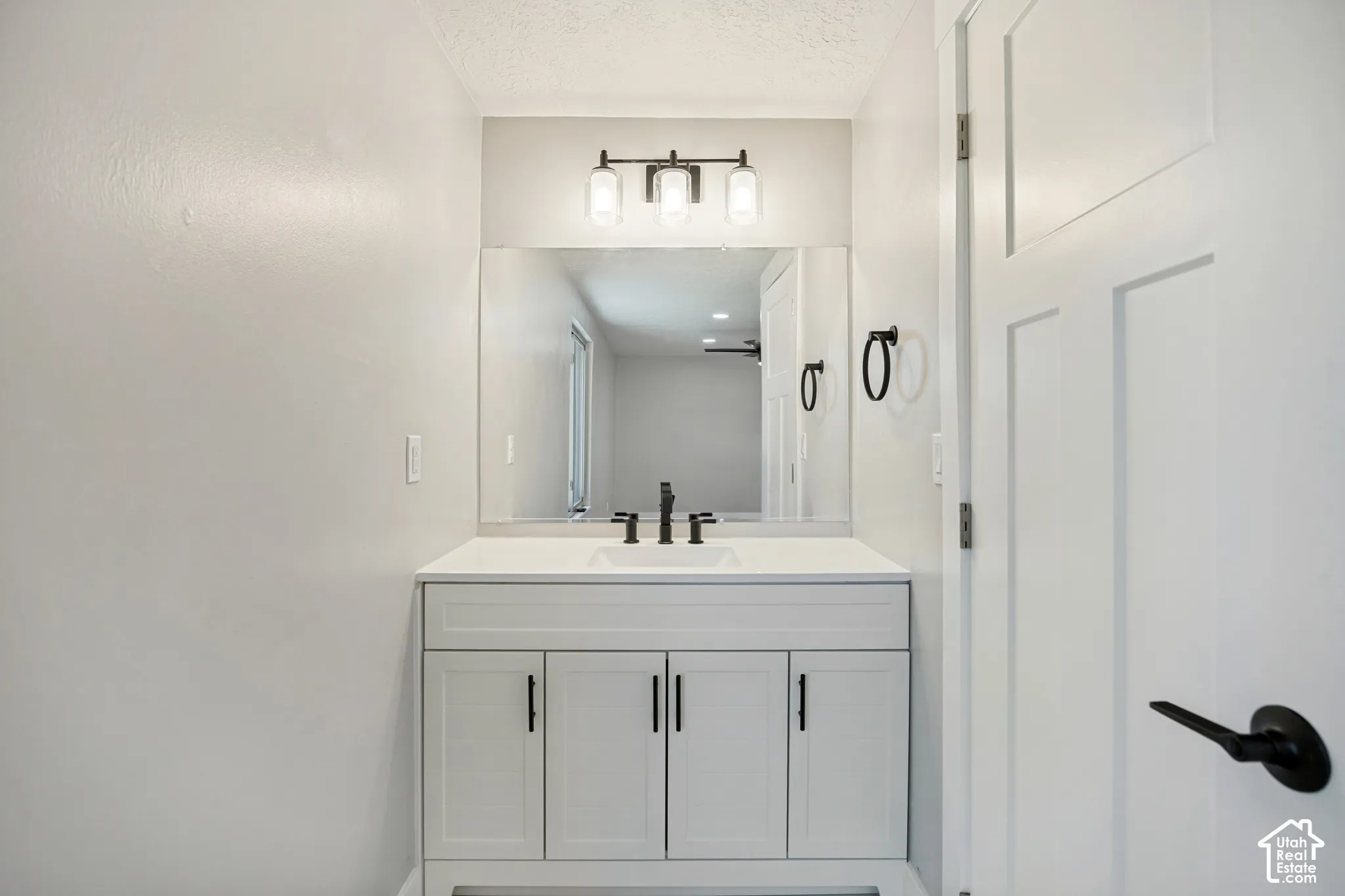 White vanity with three cabinet doors, a drop-in sink, and a black faucet