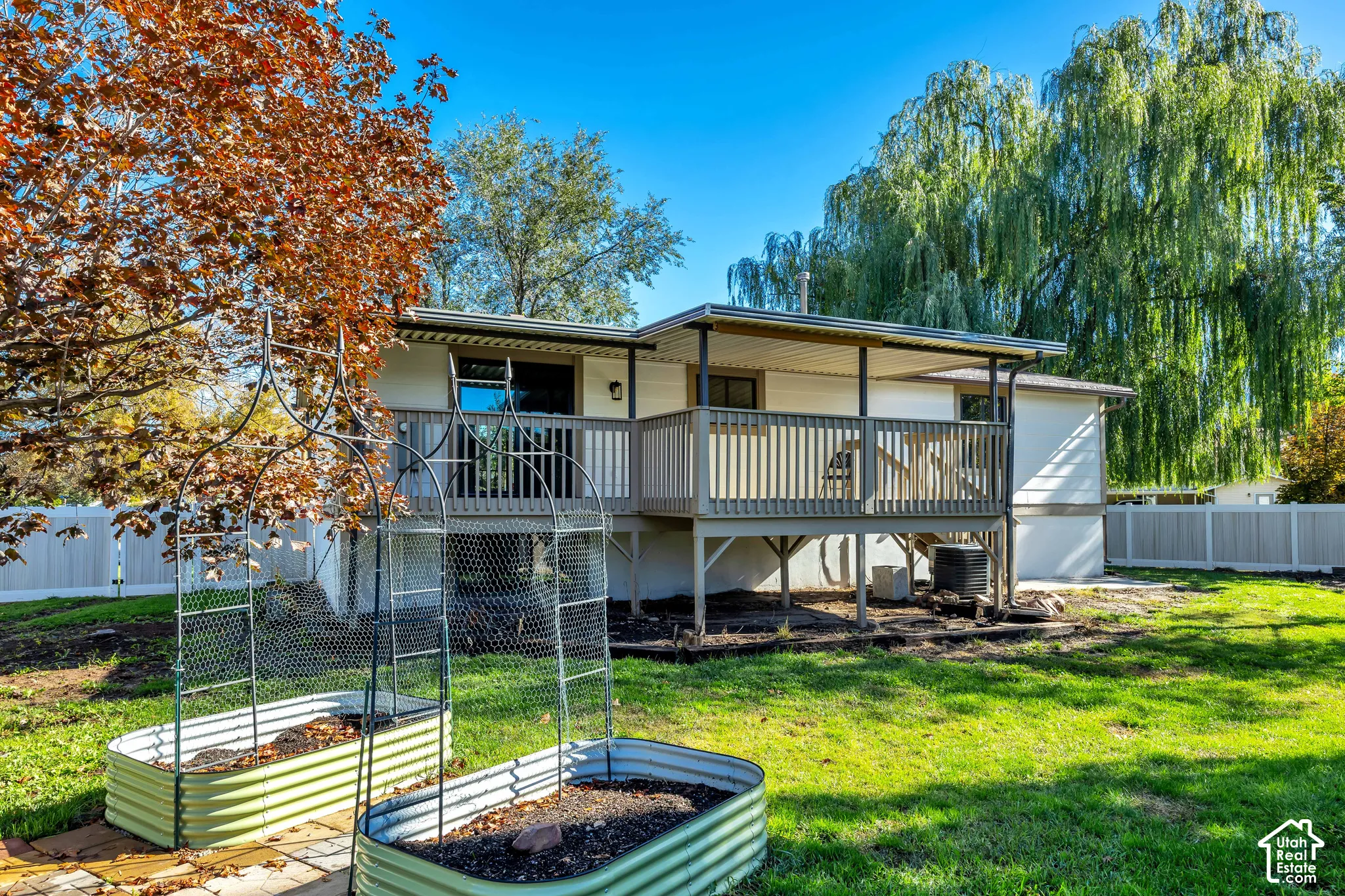 Expansive backyard with a covered deck, raised garden beds, and a white privacy fence