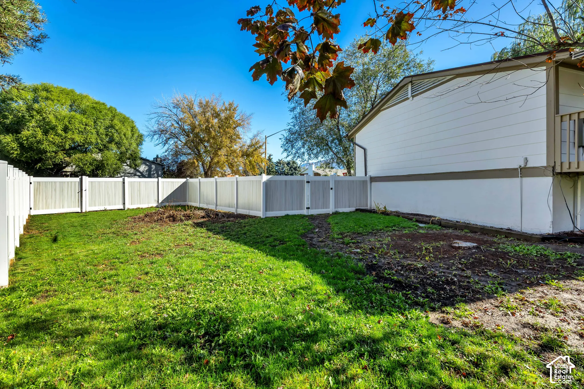 Expansive rear yard featuring green lawn, white privacy fencing, and a two-tone exterior with horizontal siding