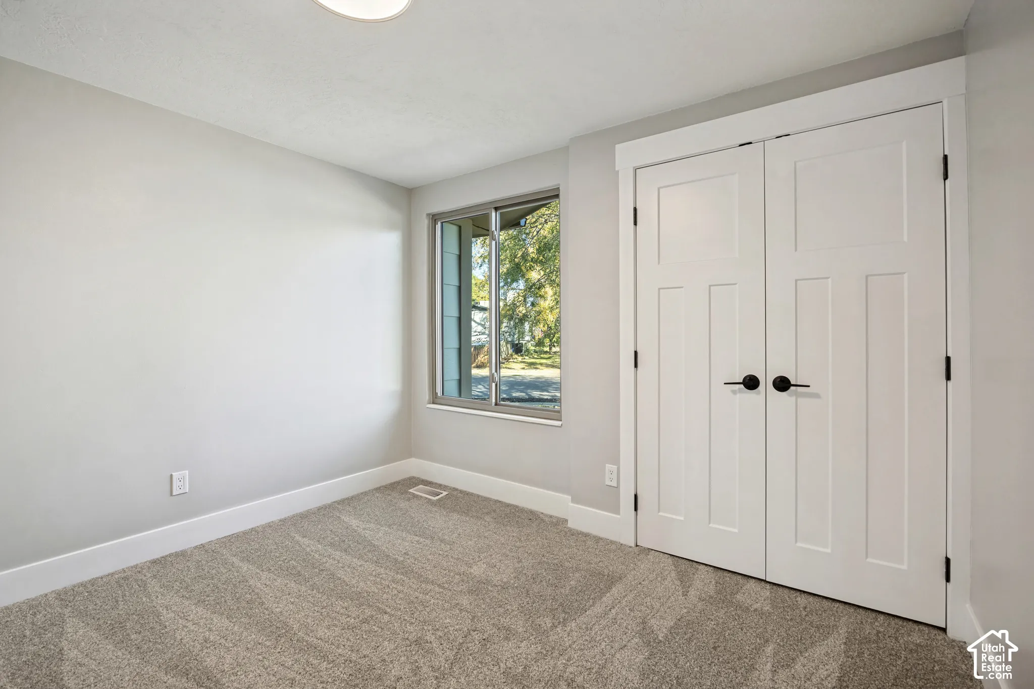 Neutral wall color, carpet flooring, a window with exterior visibility, and white paneled double doors with dark hardware