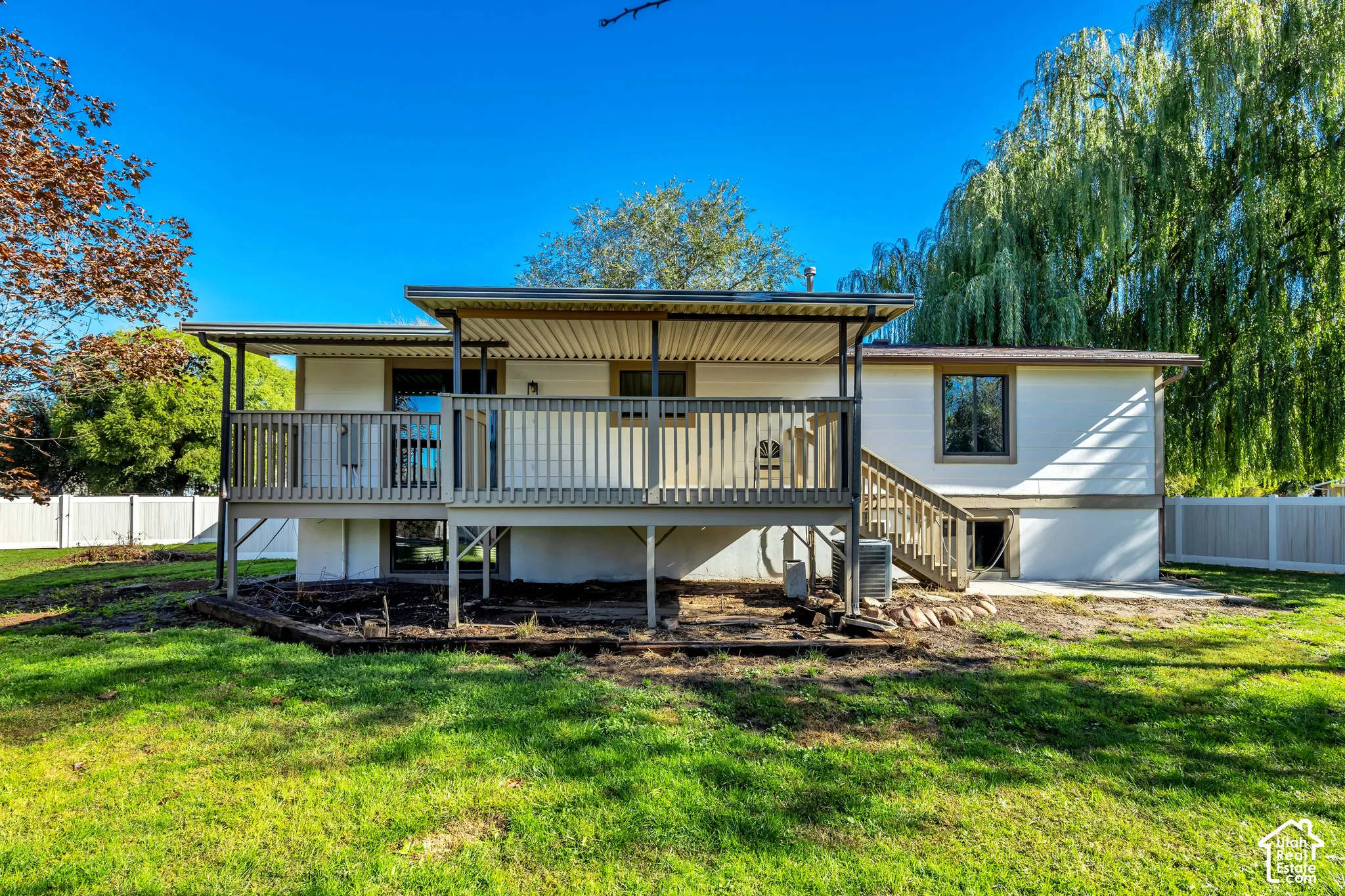 Expansive backyard featuring a covered deck, wood-tone railing, mature trees, and a privacy fence
