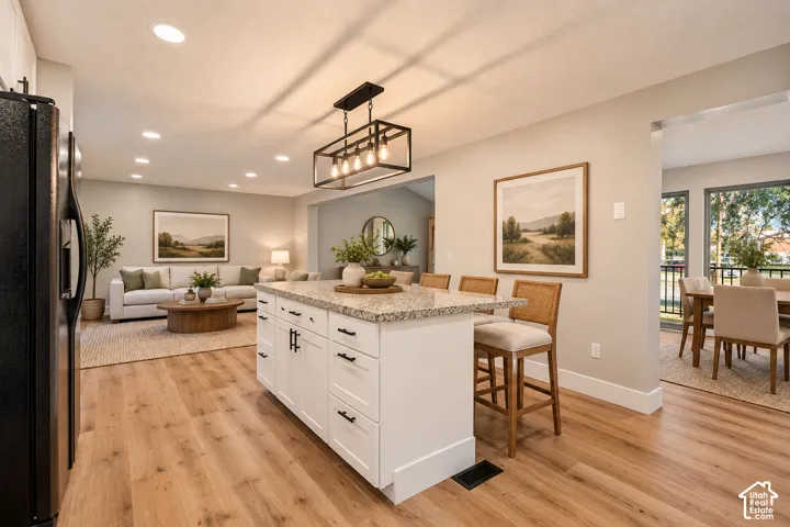 Kitchen island with granite countertop, recessed lighting, wood-finish flooring, white cabinetry with dark hardware, and a modern chandelier