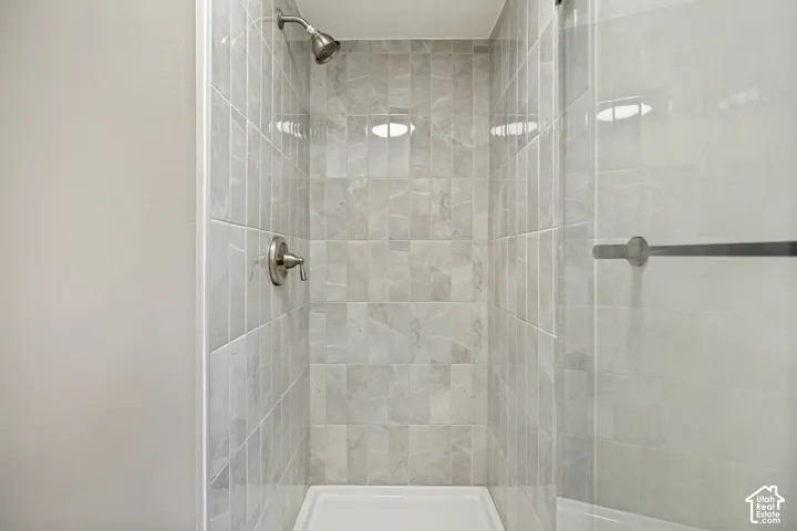 Tiled shower with brushed nickel fixtures, a glass shower enclosure, and a white shower base