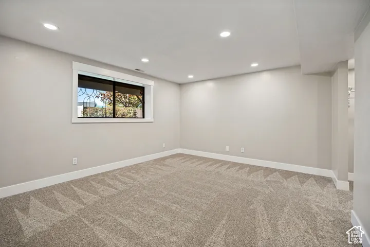 Recessed lighting, neutral wall tones, window with white trim, patterned carpeting, and white baseboards
