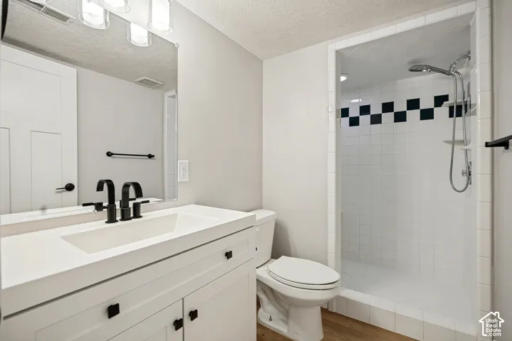 Walk-in shower with checkerboard accent tile, white vanity with integrated sink, black dual-handle faucet, and wood-finish flooring