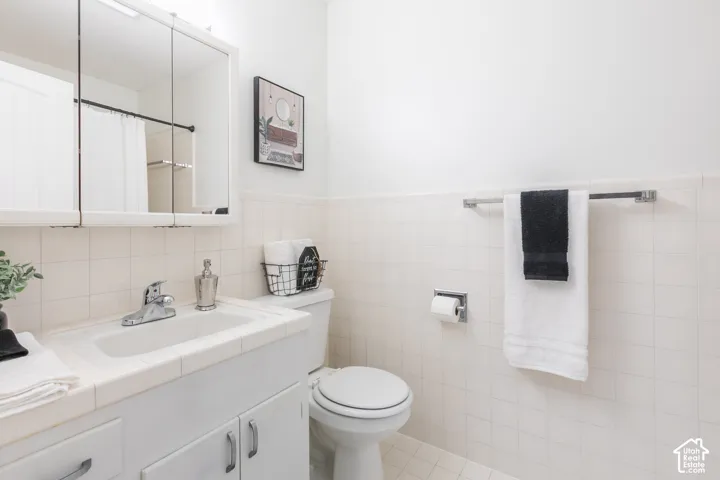 Bathroom with white tile walls, a white vanity with integrated sink, chrome faucet, and mirrored medicine cabinet