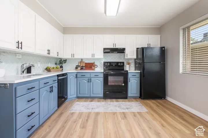 Wood-finish flooring, white upper cabinetry, blue lower cabinetry, light-toned countertops, and a full suite of black appliances