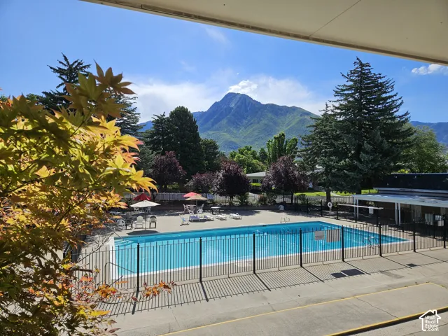 Outdoor swimming pool with black metal fencing, surrounded by mature trees and a distant mountain range