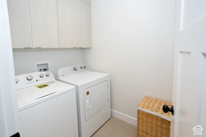 Laundry area featuring light-toned upper cabinetry, light-colored tile flooring, and white walls