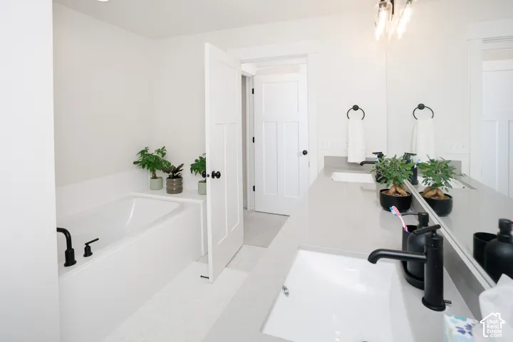 Built-in bathtub with black hardware, dual vanity with undermount sinks, extended countertop, black wall-mounted towel rings, and black framed mirror