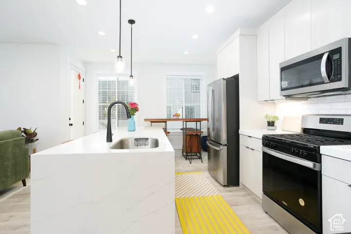Kitchen featuring an island with an integrated sink and matte black faucet, stainless steel appliances, recessed lighting, and light wood-finish flooring